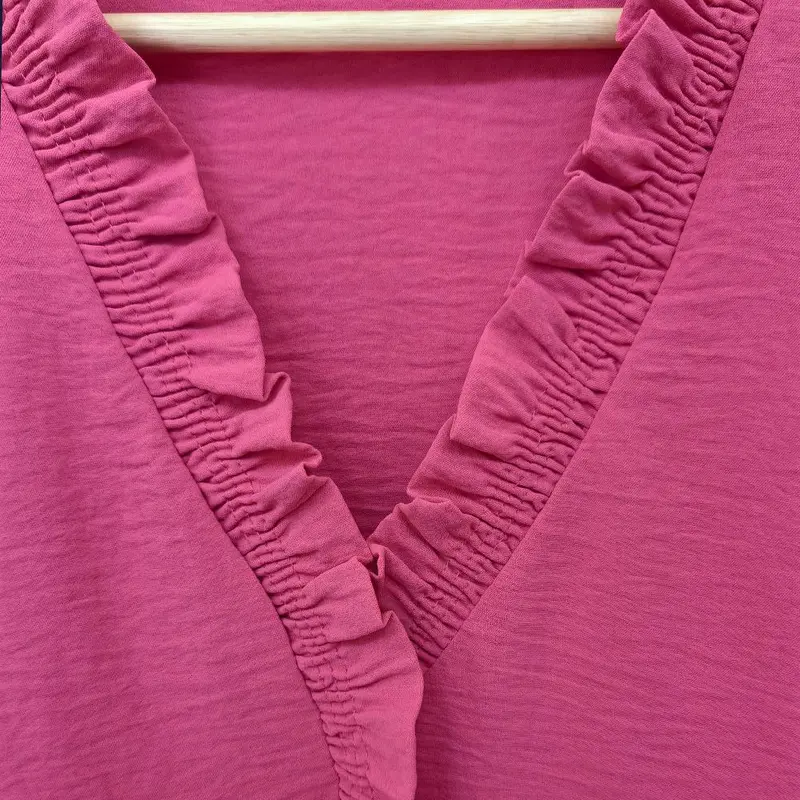 A bright pink V-neck shirt with ruffled details, featuring pleats at the cuffs and front, made of soft fabric.