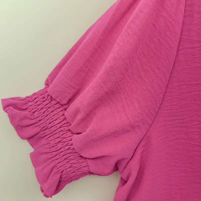 A bright pink V-neck shirt with ruffled details, featuring pleats at the cuffs and front, made of soft fabric.
