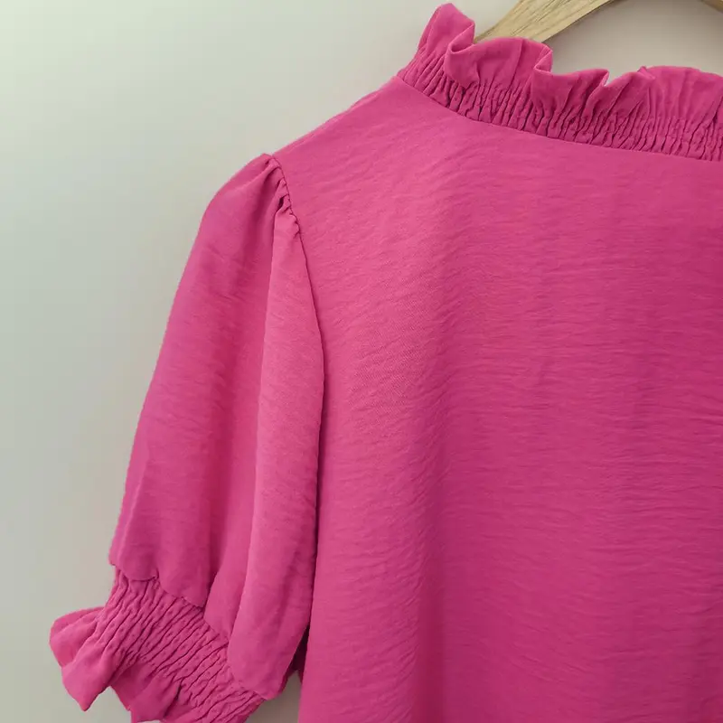 A bright pink V-neck shirt with ruffled details, featuring pleats at the cuffs and front, made of soft fabric.